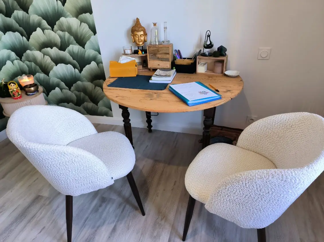 Deux fauteuils clairs face à une table de bois, devant un panneau végétal